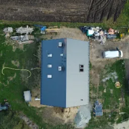 Widok z lotu ptaka na dwukolorowy dach domu z oknami dachowymi, z placem budowy wokół, w tym gruz, materiały budowlane i zaparkowane pojazdy.