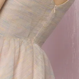 Delikatna, pastelowa sukienka z subtelnym wzorem w paski, widoczny zamek błyskawiczny z tyłu i ozdobny guzik przy szyi, na tle różowej ściany.