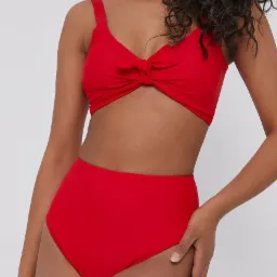 Modelka prezentuje dwuczęściowy, czerwony strój kąpielowy z wysokim stanem i wiązaniem na biuście, na jasnym tle.