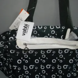 Czarno-biała torba damska Vabbi z otwartą kieszenią na zamek, widoczne metki i uchwyty, na szarym tle. Wz&oacute;r w koła i małe kwiatki.