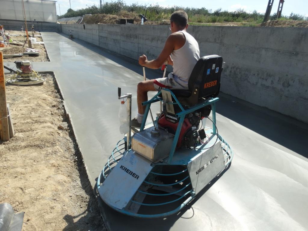 Pracownik wyrównuje świeżo wylaną posadzkę przemysłową za pomocą mechanicznej zacieraczki marki Kreber. Widoczne ślady obróbki na gładkiej, szarej powierzchni.