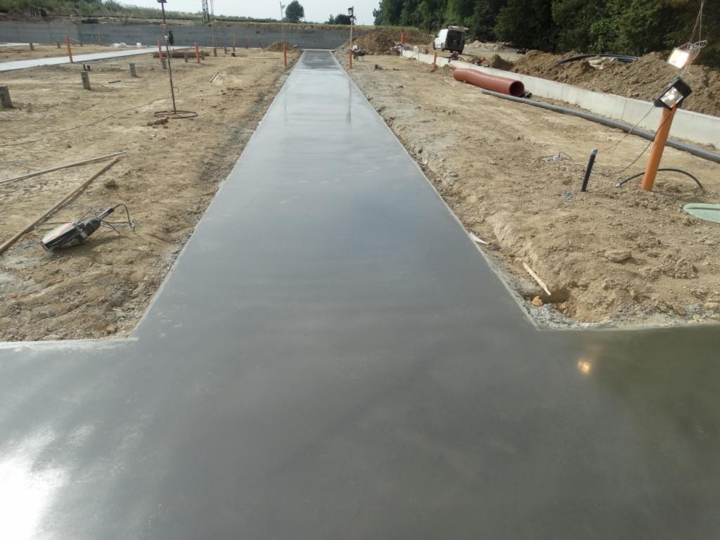 Świeżo wylana, gładka posadzka na placu budowy, widoczne narzędzia i przygotowane podłoże. Długa, szara wylewka z wyraźnymi krawędziami.