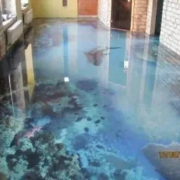 Efektowna posadzka żywiczna w odcieniach błękitu i szarości, imitująca dno morskie z rafą koralową. Błyszcząca powierzchnia odbija światło, tworząc iluzję głębi.