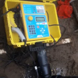 Urządzenie diagnostyczne ZK 160 PRO w żółtej obudowie, podłączone do czarnej rury z białymi czujnikami, umieszczone w wykopie ziemnym.