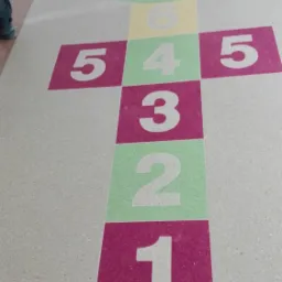 Gra w klasy z numerami 1-8 naniesiona na beżową podłogę wewnątrz budynku, widoczny fragment buta osoby stojącej obok.