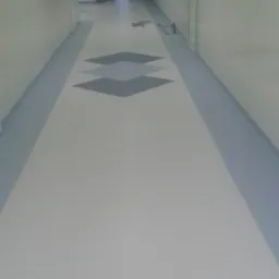 Długi korytarz w budynku publicznym z nową, jasną podłogą z szarymi geometrycznymi wzorami. Na podłodze leżą narzędzia. Ściany pomalowane w odcieniach zieleni i bieli.