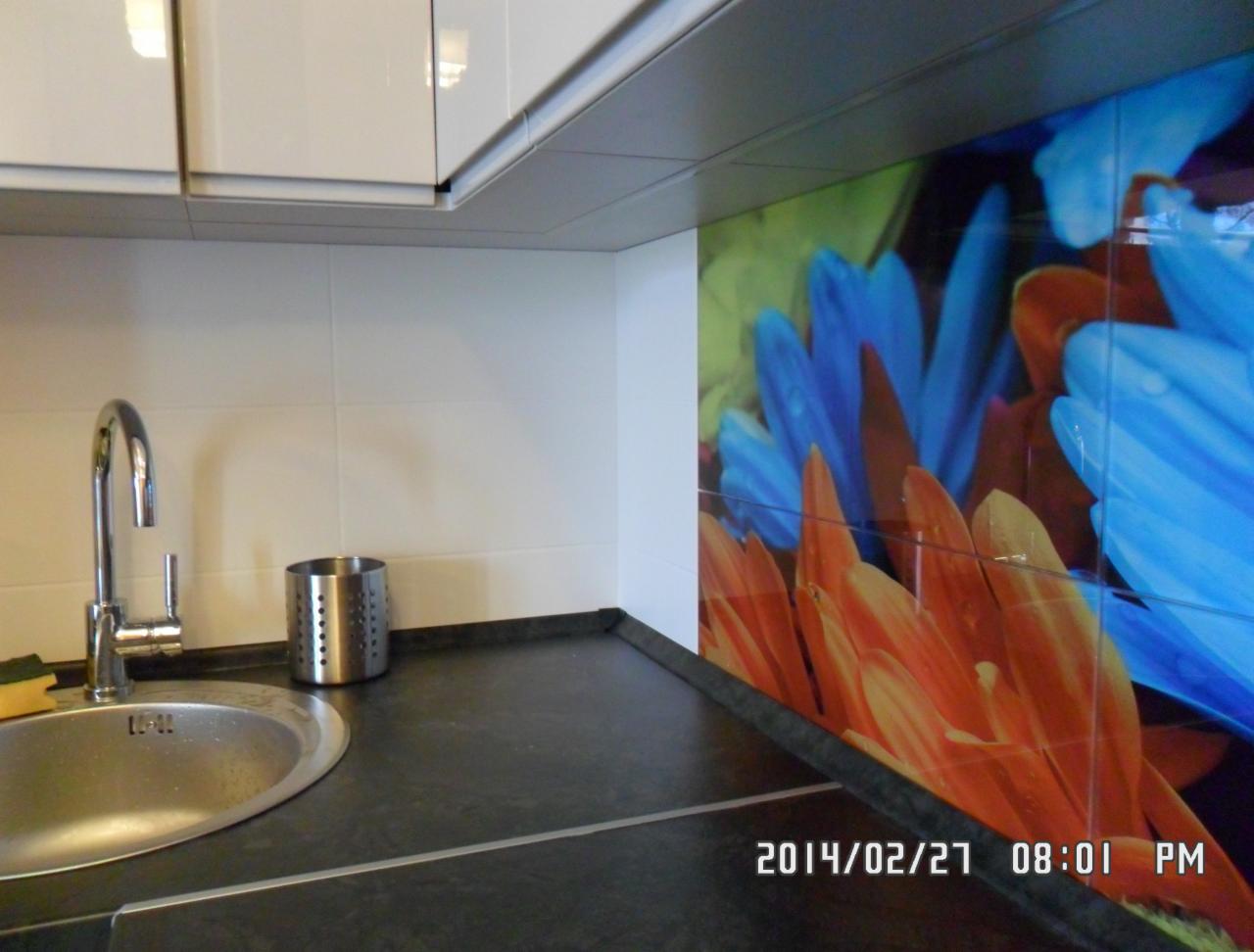 Błyszcząca, nowoczesna kuchnia z chromowaną baterią, ciemnym blatem i ścianą z motywem kwiatowym. Białe szafki wiszące.