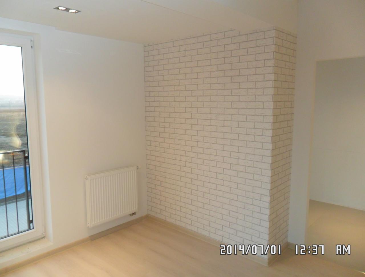 Białe wnętrze po remoncie: ściana z tapetą imitującą cegłę, jasna podłoga, okno z widokiem na zewnątrz i grzejnik. Minimalistyczny design i świeżość.