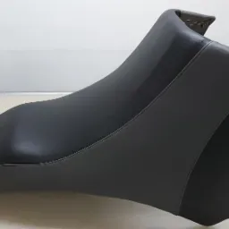 Czarne, skórzane siedzisko motocyklowe, świeżo po obszyciu, z widocznymi zszywkami na krawędzi, leżące na stole w warsztacie.