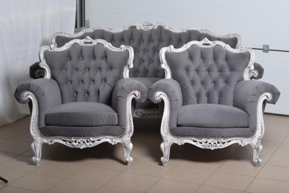 Szary, welurowy komplet wypoczynkowy w stylu Ludwika XVI, składający się z sofy i dwóch foteli z ozdobnymi, srebrnymi ramami i pikowanym oparciem.