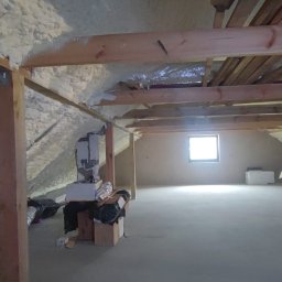 CELS Mariusz Butkiewicz - Poddasze z drewnianą konstrukcją dachu, częściowo ocieplone pianką PUR, widoczne instalacje wentylacyjne i okno.