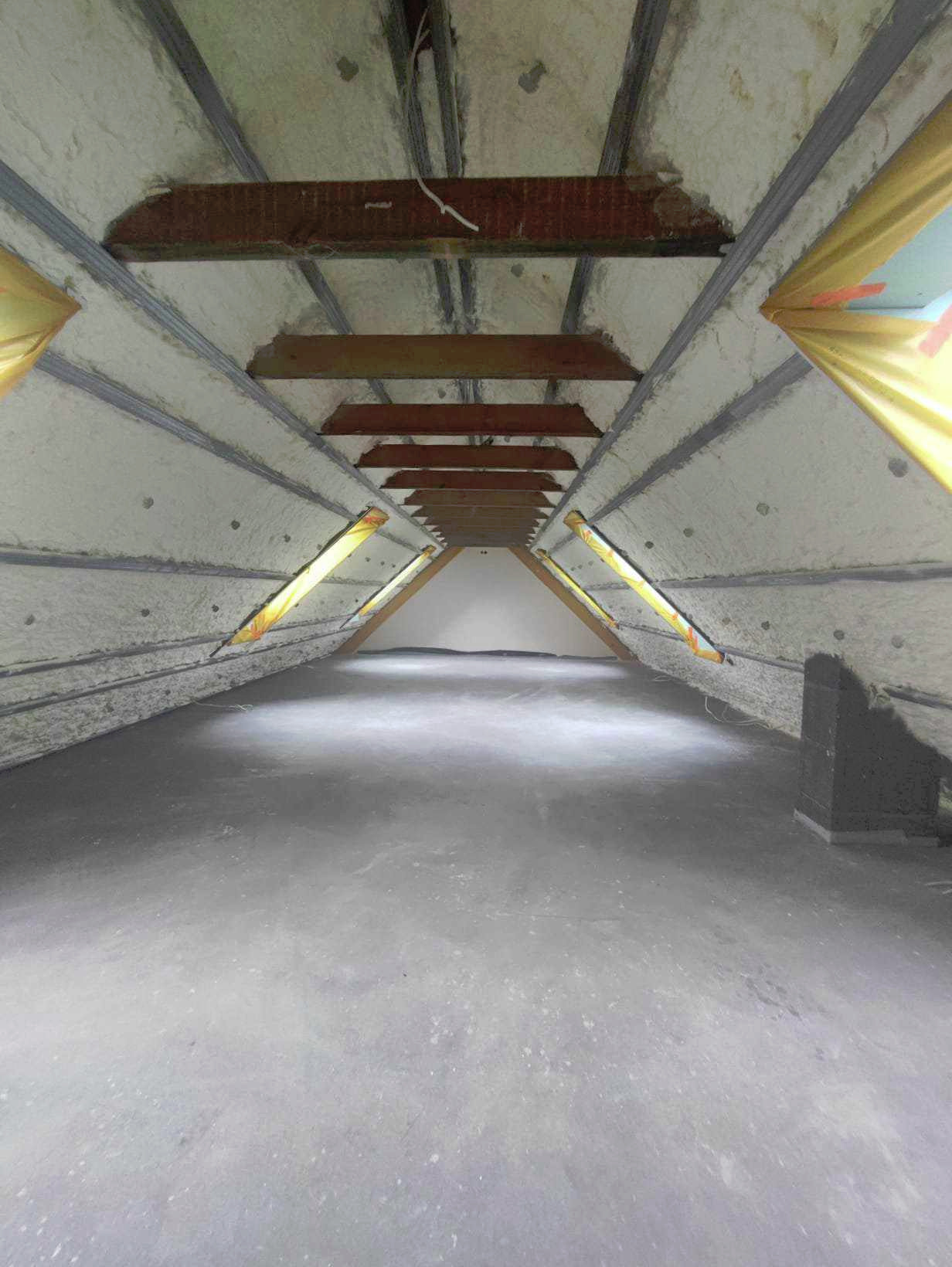 Poddasze po ociepleniu pianką, widoczne drewniane belki i szare profile, surowy beton na podłodze.