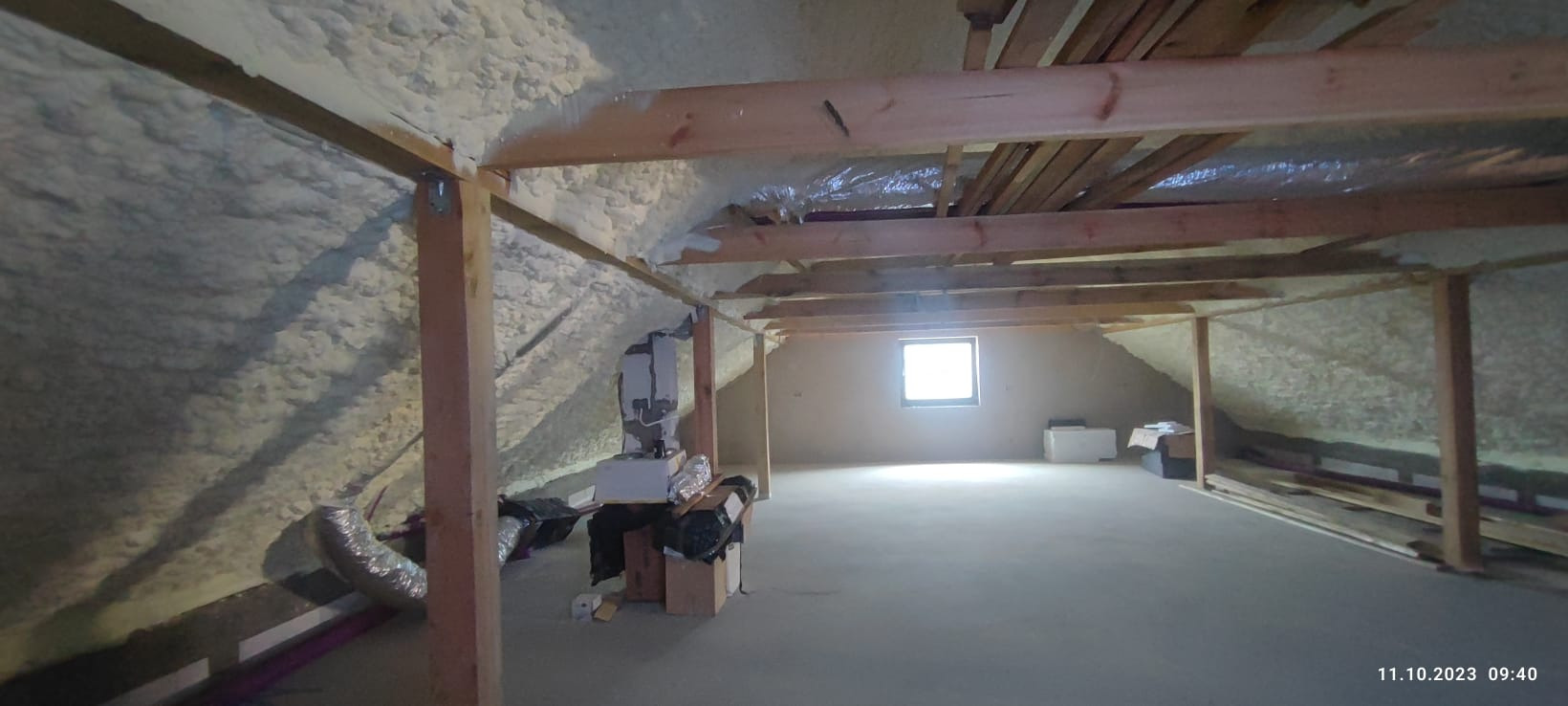 Poddasze z drewnianą konstrukcją dachu, częściowo ocieplone pianką PUR, widoczne instalacje wentylacyjne i okno.