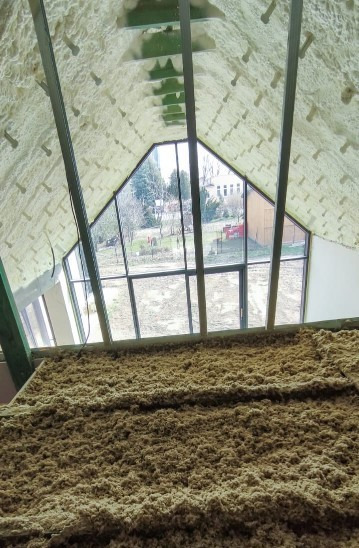 Poddasze z oknem, ocieplone pianką PUR na dachu i wełną mineralną na podłodze, widok na ogród z budynkiem w tle.