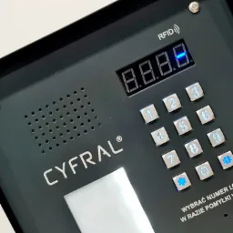 Panel wejściowy z klawiaturą numeryczną i czytnikiem RFID firmy Cyfral w kolorze antracytowym, zainstalowany w Zgierzu, z podświetlanymi przyciskami i wyświetlaczem LED.