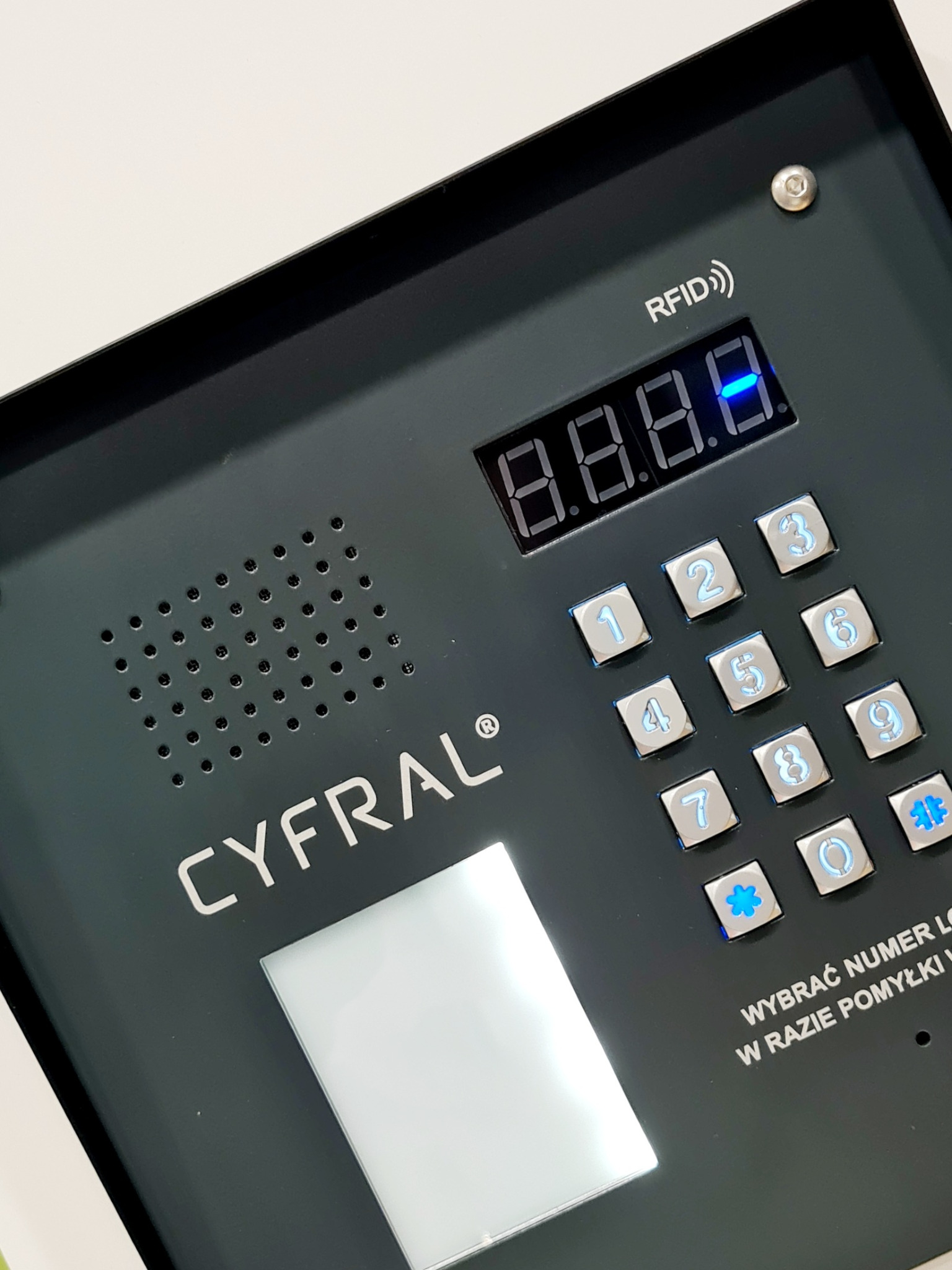 Panel wejściowy z klawiaturą numeryczną i czytnikiem RFID firmy Cyfral w kolorze antracytowym, zainstalowany w Zgierzu, z podświetlanymi przyciskami i wyświetlaczem LED.