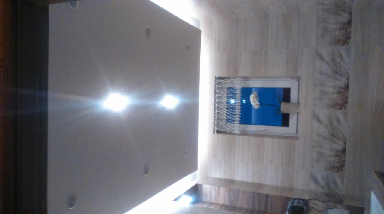 Nowoczesne wnętrze: gładki sufit z oświetleniem punktowym, dekoracyjna ściana z motywem kwiatowym i okno z zasłonką. Ujęcie z dołu, podkreślające detale wykończenia.