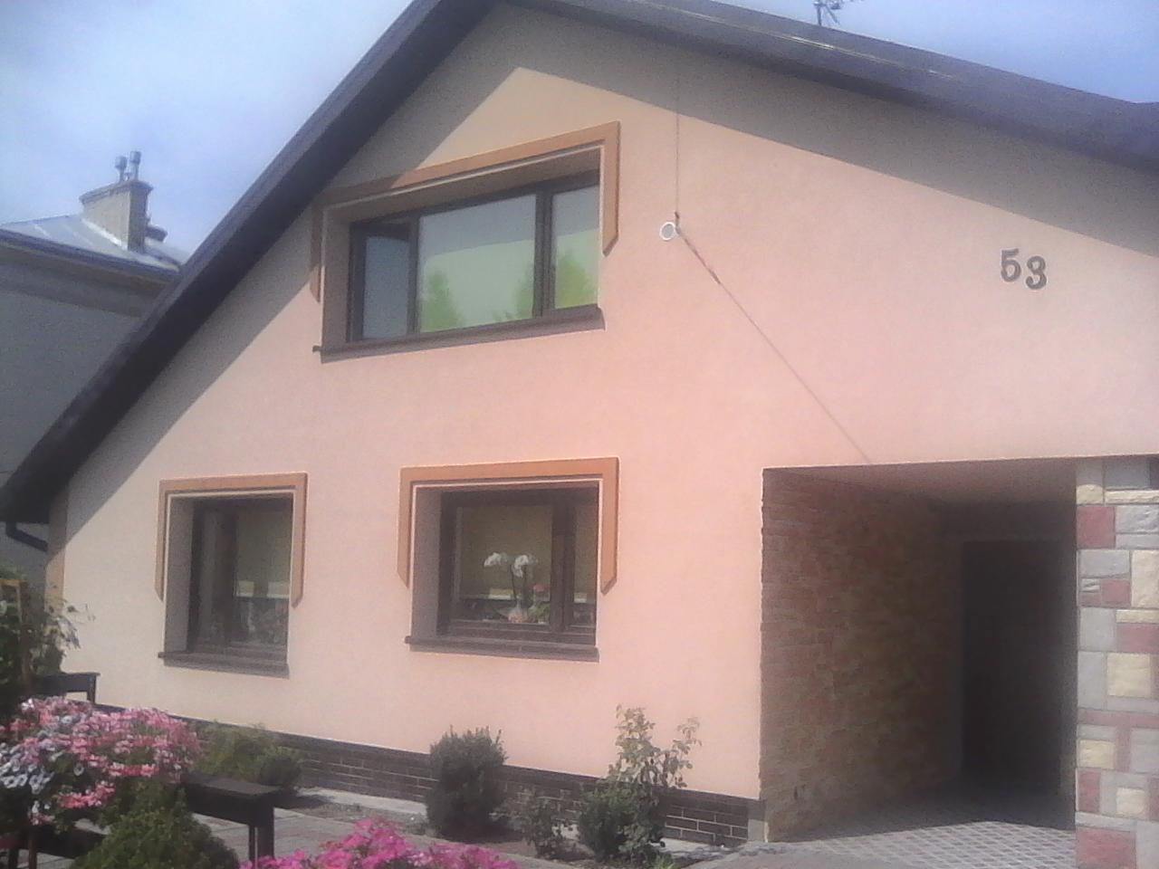 Dom jednorodzinny po remoncie elewacji z oknami w ciemnych ramach i numerem 53 na ścianie, widoczne kwiaty i garaż.