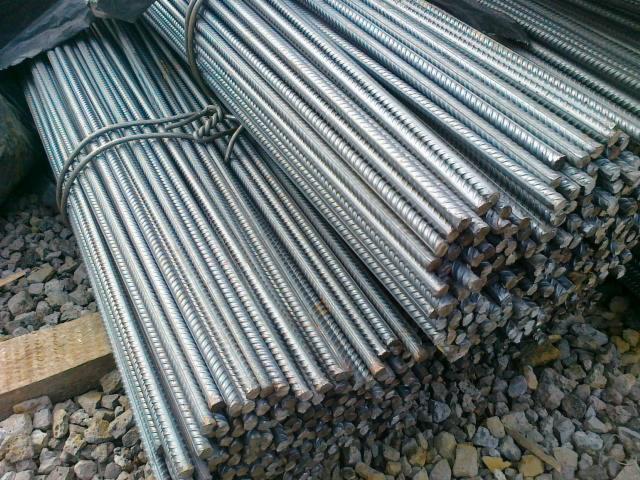 Dwa pęki żebrowanych prętów na tle kamieni. Pręty związane drutem. Widoczne przekroje poprzeczne prętów i żebrowana powierzchnia.