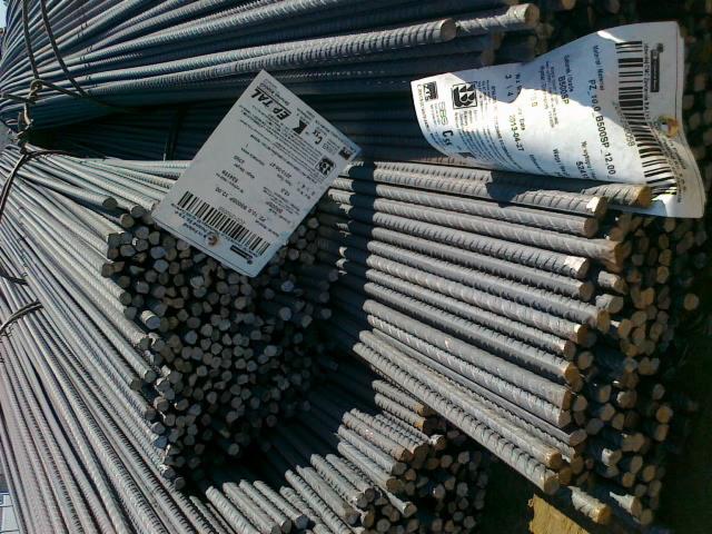 Wiązki żebrowanych prętów zbrojeniowych, spięte drutem, z etykietami producenta. Widoczne przekroje poprzeczne i podłużne prętów.