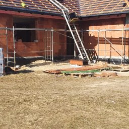 M&M BLACHARSTWO-DEKARSTWO MAREK MALISKA - Budowa domu jednorodzinnego w trakcie krycia dachu dachówką ceramiczną, widoczny podnośnik do transportu materiałów budowlanych na dach.