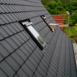 Nowy, grafitowy dach z dach&oacute;wki ceramicznej z zamontowanymi oknami dachowymi; widok z dołu na tle zieleni.