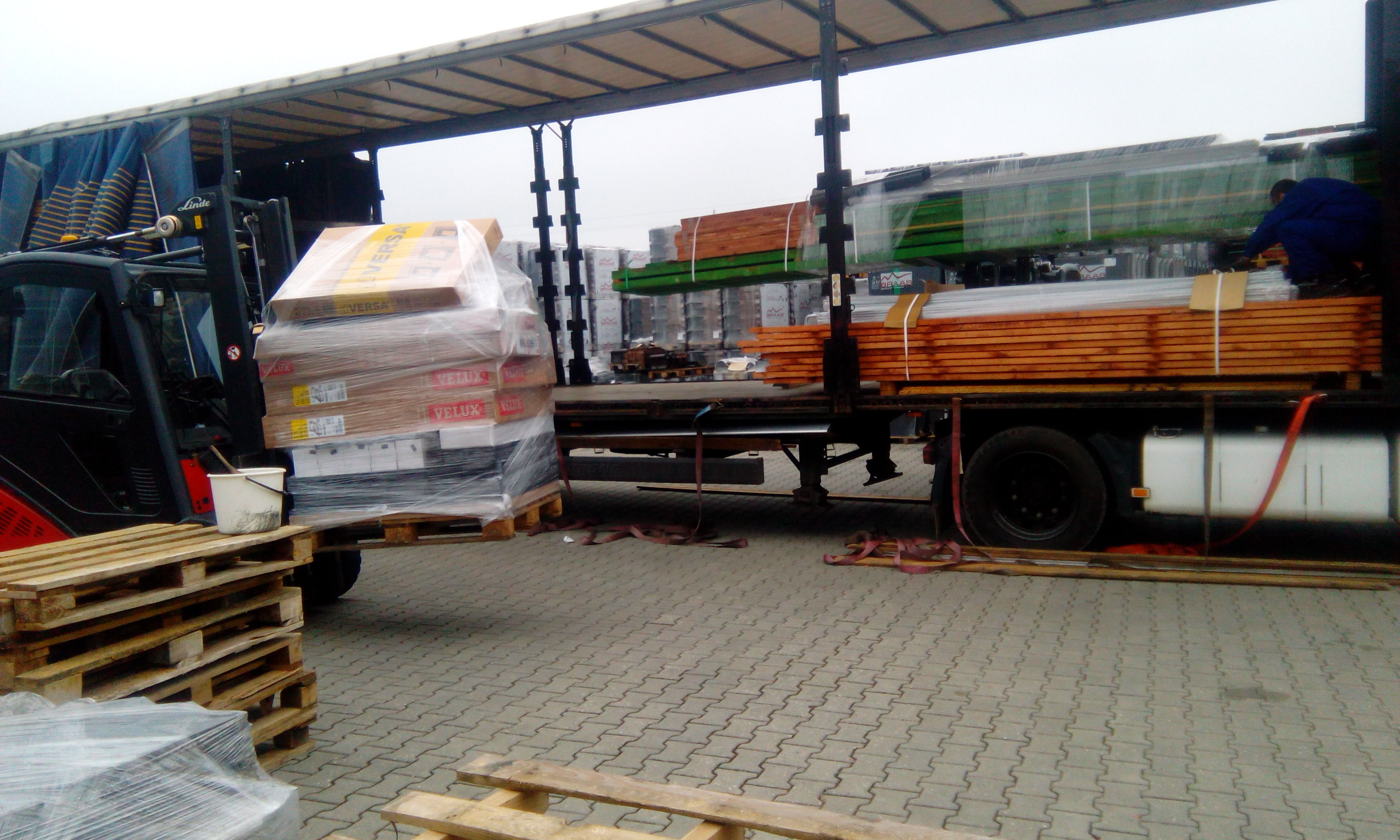 Rozładunek transportu drewna i okien dachowych Velux za pomocą wózka widłowego na placu budowy.