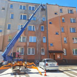 PHU Pro-Clean - Pracownik na podnośniku koszowym czyści elewację wielopiętrowego budynku, widoczne zacieki po spływającej wodzie, na dole zaparkowany samochód i van firmy Pro-Clean z reklamą usług.