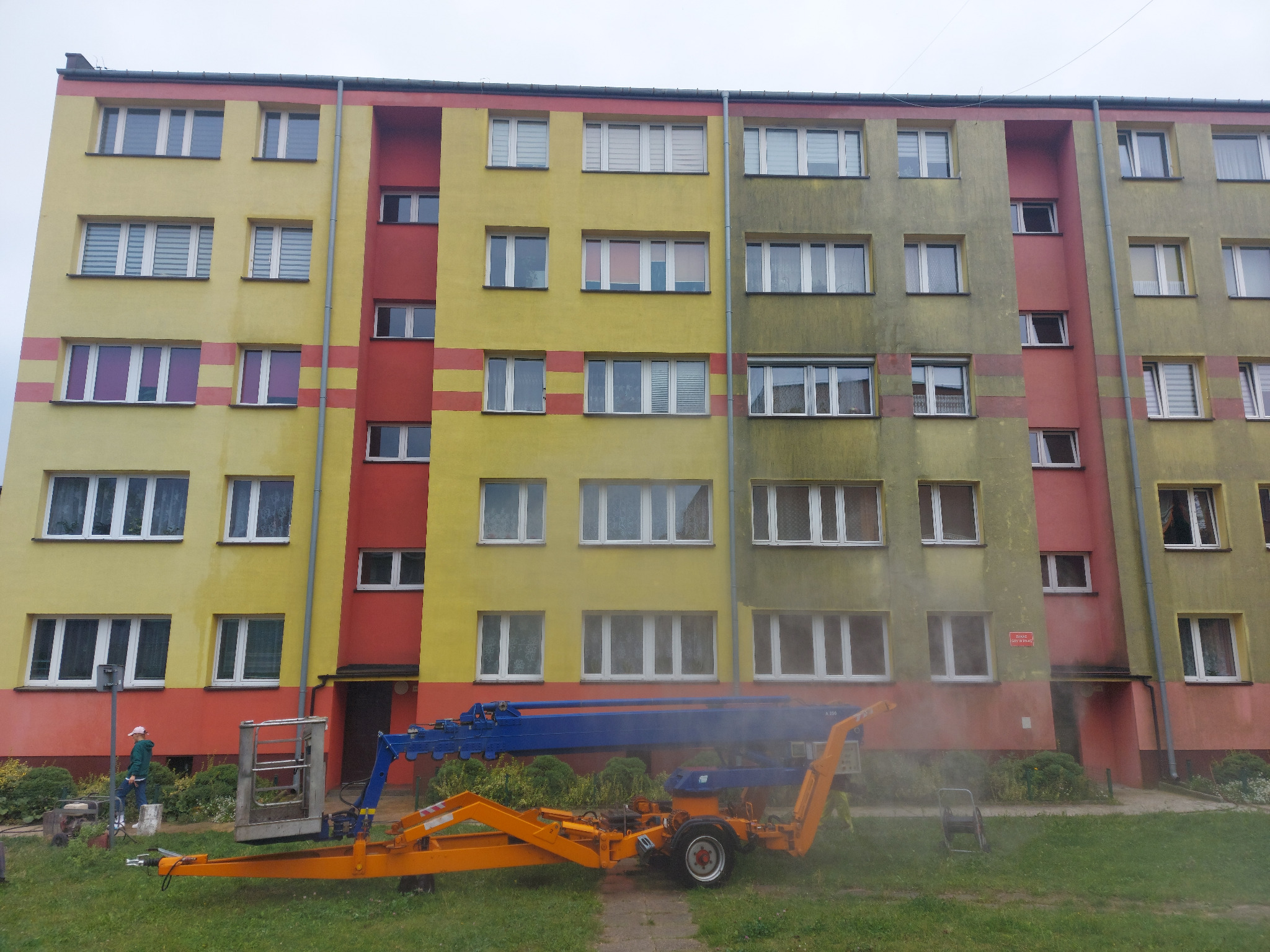 Czyszczenie fragmentu elewacji bloku mieszkalnego z użyciem podnośnika koszowego; widoczna różnica w kolorze pomiędzy umytą a brudną powierzchnią.