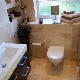 Jasna łazienka z beżowymi płytkami, umywalką z ciemnymi szafkami, toaletą i grzejnikiem drabinkowym, dekorowana trawą pampasową i ręcznikami przy oknie.