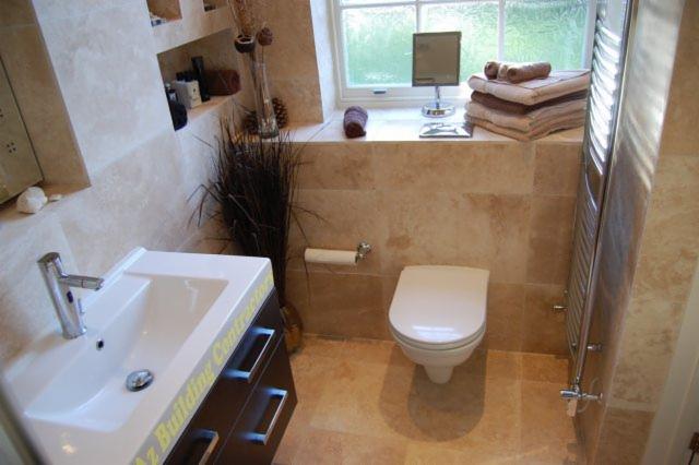 Jasna łazienka z beżowymi płytkami, umywalką z ciemnymi szafkami, toaletą i grzejnikiem drabinkowym, dekorowana trawą pampasową i ręcznikami przy oknie.