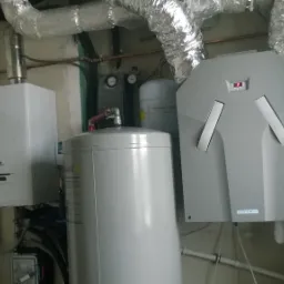 Kotłownia z zamontowanym kotłem gazowym, zbiornikiem buforowym i rekuperatorem z widocznymi przewodami wentylacyjnymi.