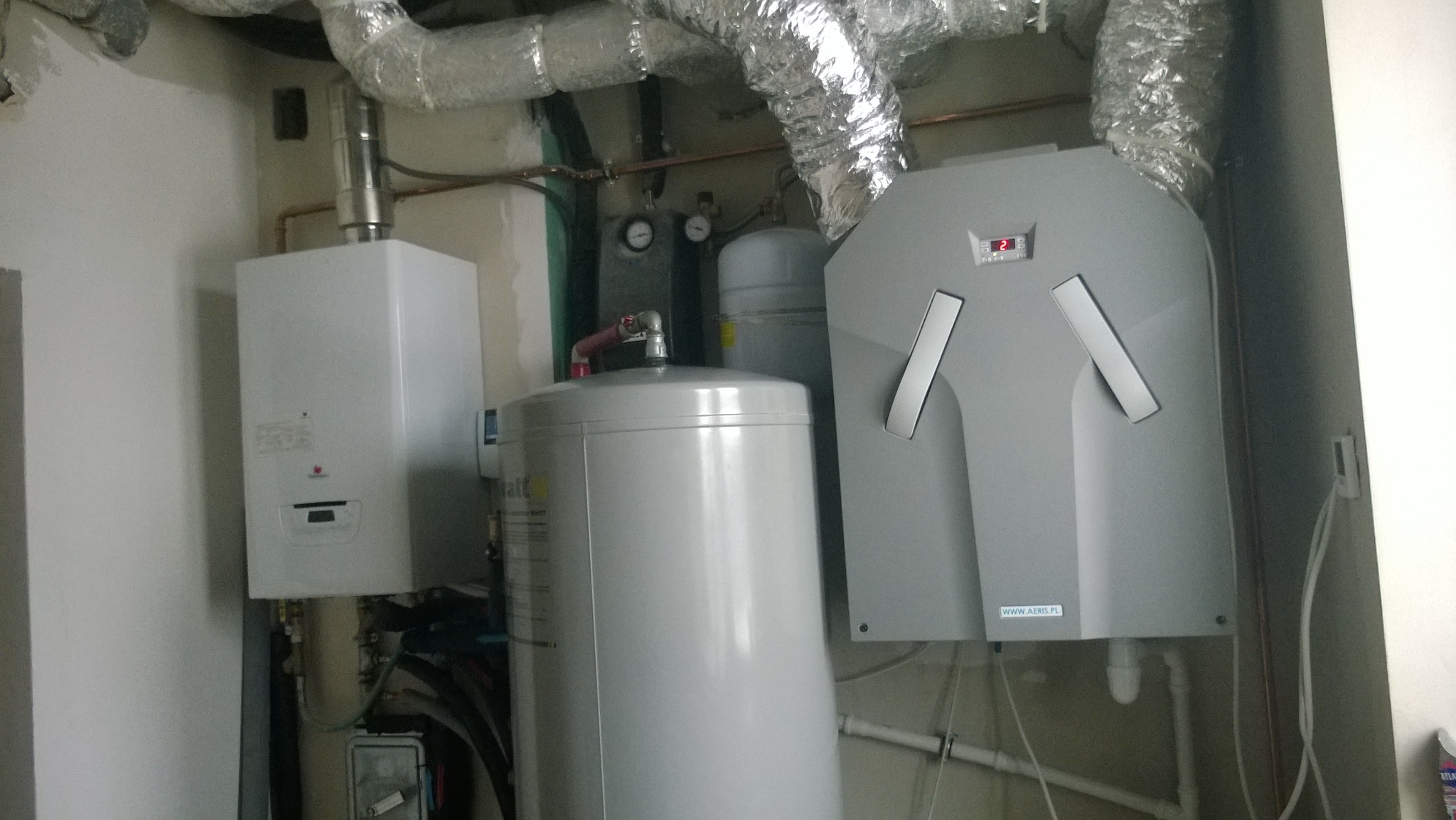 Kotłownia z zamontowanym kotłem gazowym, zbiornikiem buforowym i rekuperatorem z widocznymi przewodami wentylacyjnymi.