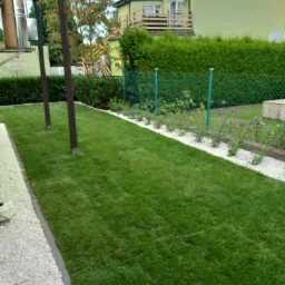 Świeżo założony trawnik z rolki, obrzeża z białego grysu, rabata kwiatowa z białym kamieniem, siatka ogrodzeniowa w tle.