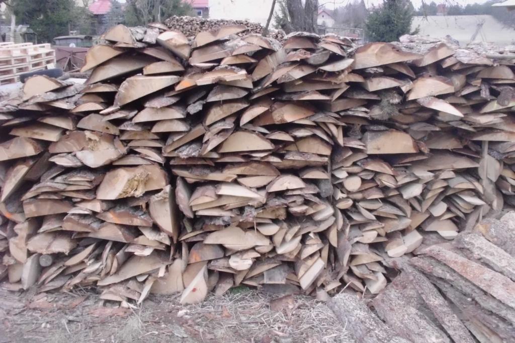 Stos pociętego drewna kominkowego z korą, ułożonego w równy rząd na zewnątrz, z paletami w tle i fragmentami kory na ziemi.