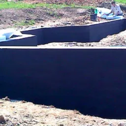 Zaizolowane fundamenty domu w ziemi, widoczna osoba pracująca na dalszym planie, przygotowanie do dalszych etapów budowy.