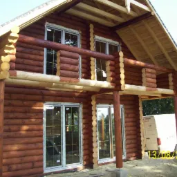 Dom z bali z białymi oknami, widoczne z zewnątrz, z datą 13/08/2013. Charakterystyczna konstrukcja z bali drewnianych i jasne wykończenie.