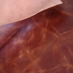 Fragment brązowej skóry naturalnej z widoczną fakturą i delikatnym połyskiem, częściowo podwiniętej, ukazującej jaśniejszy spód.