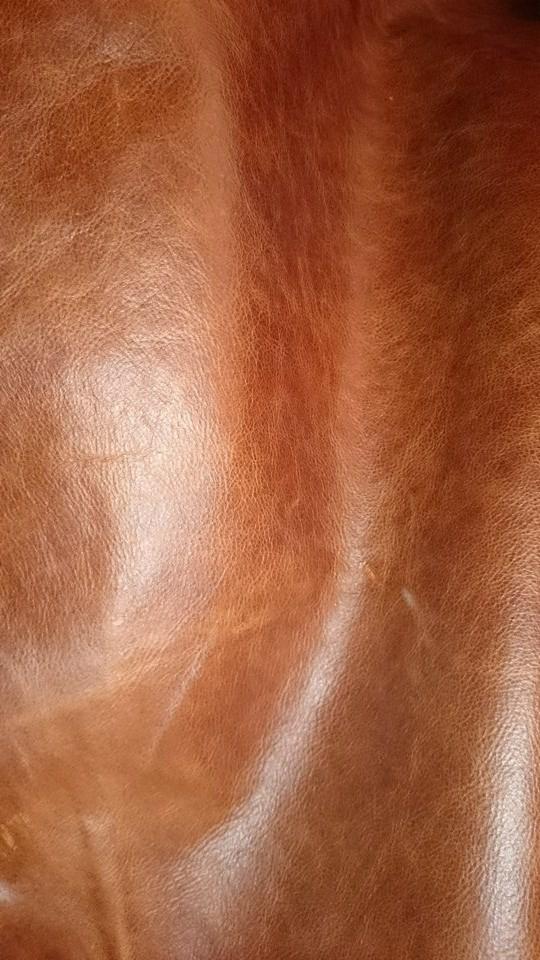 Zbliżenie na brązową, naturalną skórę. Widoczne delikatne zmarszczki i faktura materiału, podkreślone przez subtelne światło. Idealne do tapicerki meblowej.