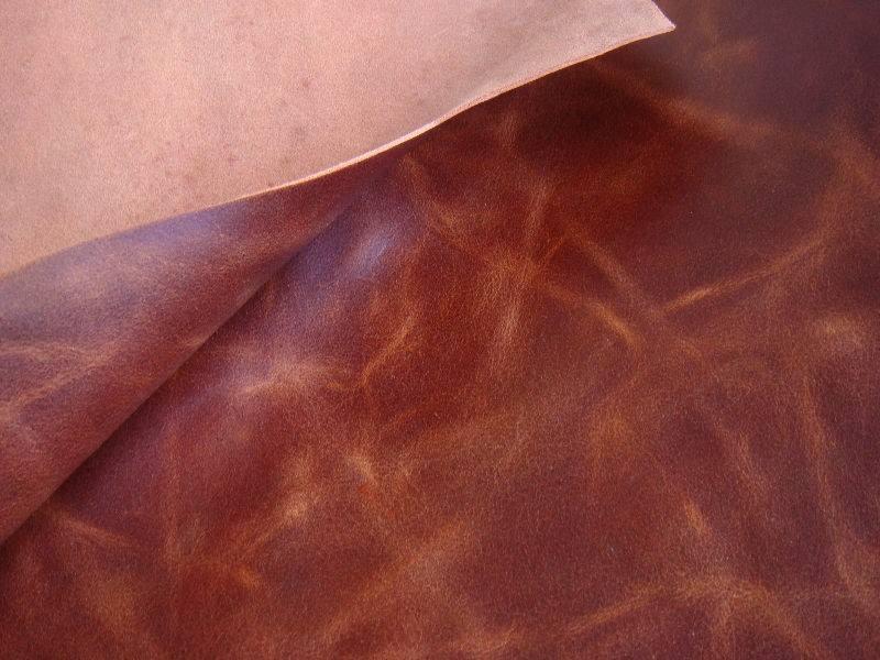 Fragment brązowej skóry naturalnej z widoczną fakturą i delikatnym połyskiem, częściowo podwiniętej, ukazującej jaśniejszy spód.