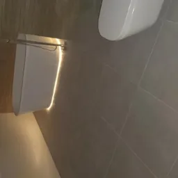 Nowoczesny wideofon z podświetleniem LED zamontowany na ścianie z szarych płytek.