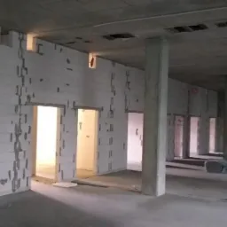 Surowy stan wnętrza budynku w trakcie budowy: ściany z betonu komórkowego z otworami drzwiowymi, betonowe kolumny nośne, surowy betonowy strop.