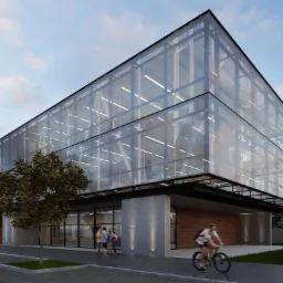 Nowoczesny, dwukondygnacyjny budynek usługowy z przeszkloną fasadą, widoczny z perspektywy ulicy z przechodniami i rowerzystą. Minimalistyczna architektura.