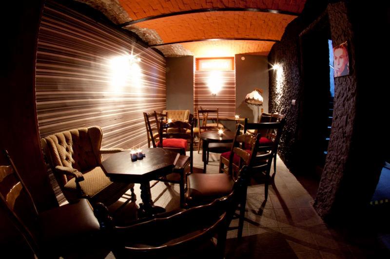 Wnętrze klubu w stylu retro z ceglanym sklepieniem, tapetą w paski, drewnianymi meblami i nastrojowym oświetleniem świecami na stolikach.