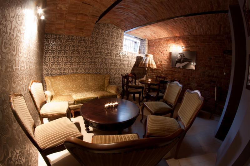 Klimatyczne wnętrze klubu w stylu retro z ceglanym sklepieniem, wzorzystymi tapetami, okrągłym drewnianym stolikiem ze świecami i meblami w stylu vintage.