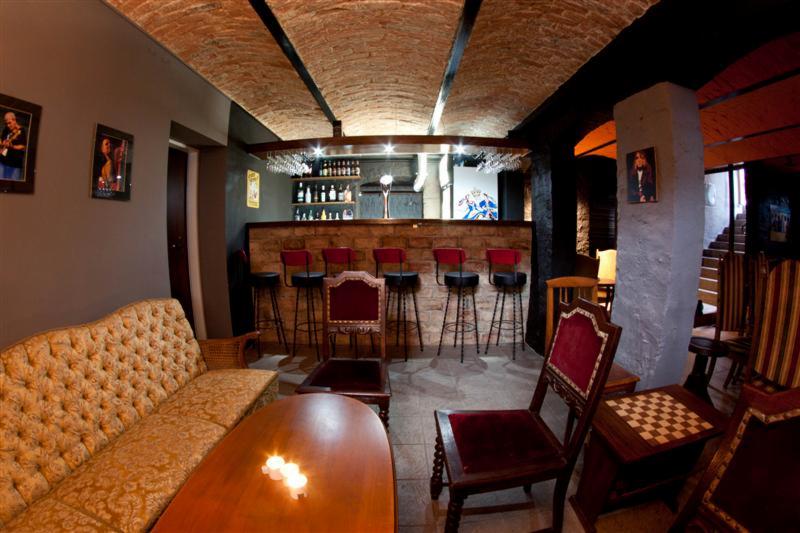 Wnętrze klubu w stylu retro z ceglanym sklepieniem, barem z czerwonymi krzesłami, sofą w stylu vintage i stolikiem ze świecami.