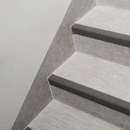 Schody pokryte szarą wykładziną z ciemnoszarymi listwami antypoślizgowymi na krawędziach stopni, widok z góry.