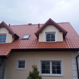 Dom jednorodzinny z nowym, błyszczącym dachem z dachówki ceramicznej w odcieniach czerwieni i brązu, z oknami dachowymi i rynnami w kolorze grafitowym.