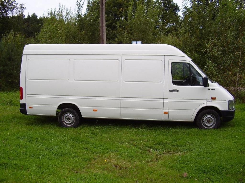 Biały samochód dostawczy na trawie przed drzewami. Widok z boku, lekko z góry. Detale: model LT35, relingi dachowe. Zdjęcie wykonane w dzień.