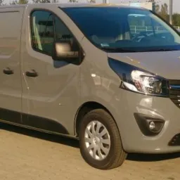 Szary samochód dostawczy Opel Vivaro zaparkowany na betonowym placu, widok z przodu i boku, z widocznymi detalami karoserii i felgami aluminiowymi.